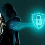Persoană în hanorac cu glugă ținând un telefon, simbolizând amenințările și protecția în securitatea cibernetică.